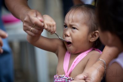 Marikina, Philippines - An unhappy girl takes a spoonful of medicine at makeshift health clinic.  Canon 5D II, 180mm, 1/80 @ f3.2, ISO 200, LowePro DZ200