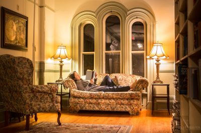 A woman curls up to read an old classic novel on an overstuffed sofa in the upper hall library of the Blomidon Inn, Wolfville, Nova Scotia.